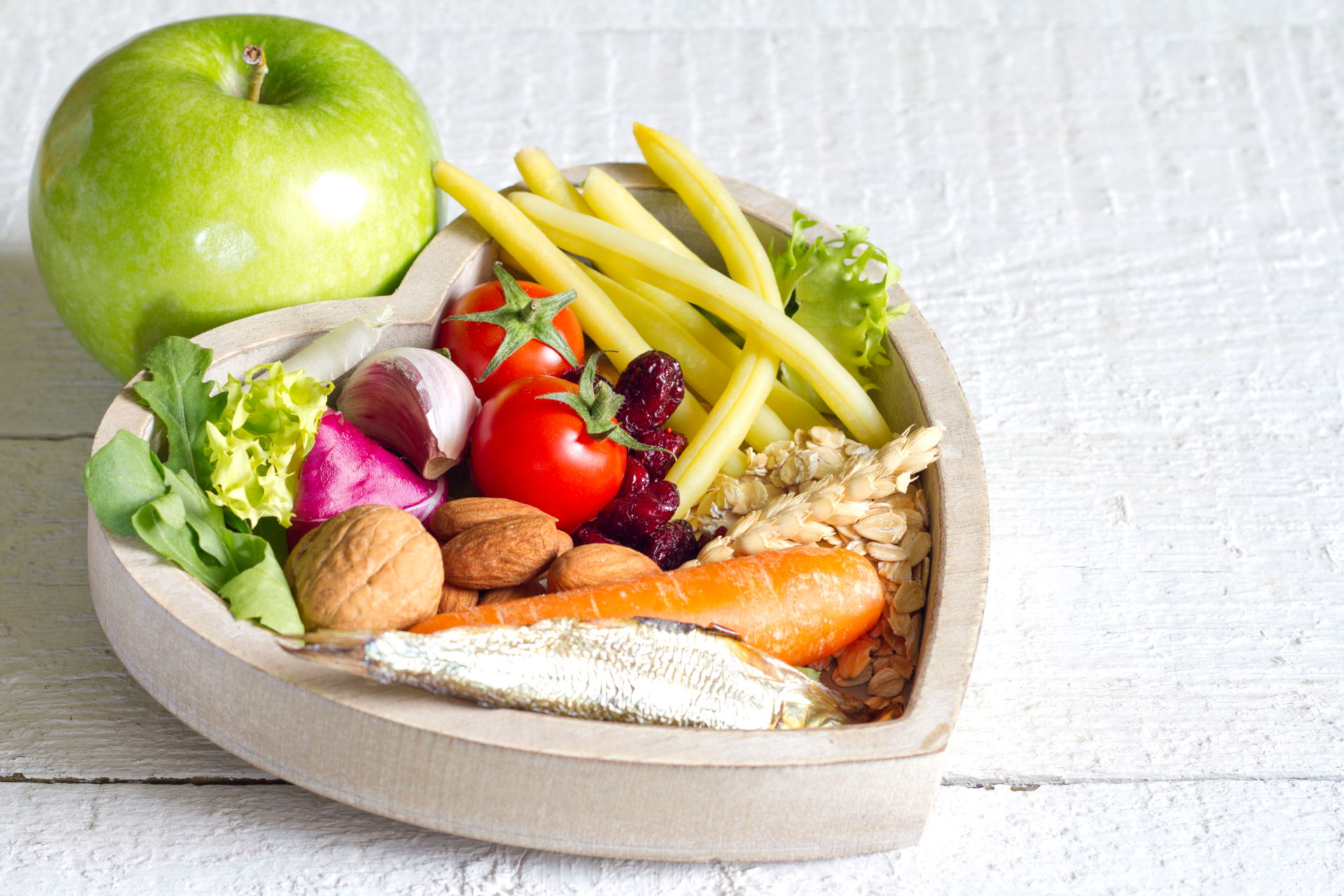 A Heart Shaped Bowl Filled With Vegetables With An Apple By The Side