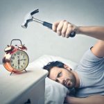 Man Hitting Alarm Clock With A Hammer As He Tries To Sleep