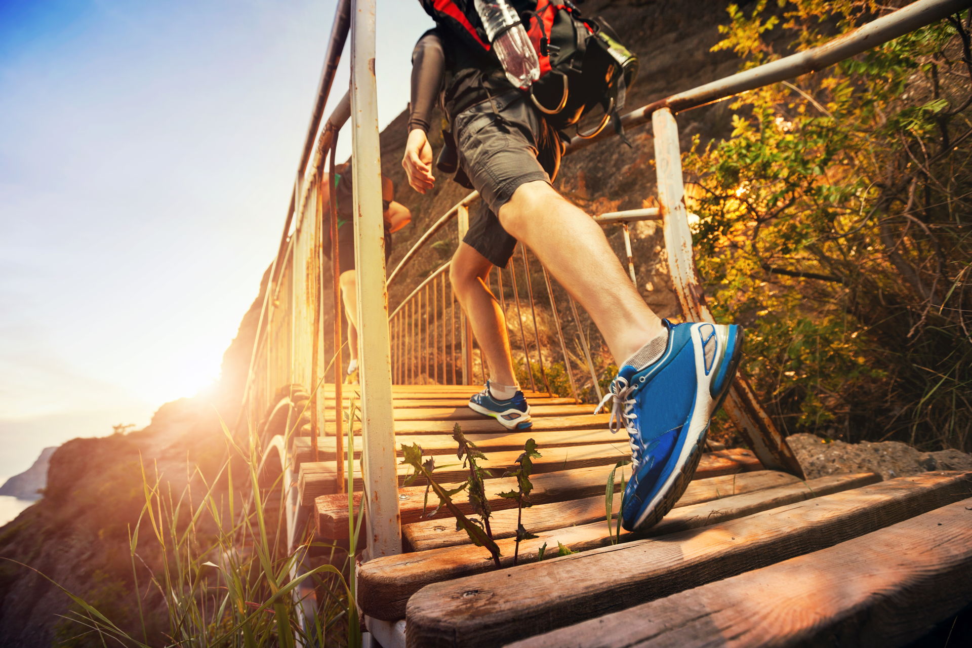 Man Walking Accross A Bridge With The Sun Shining In The Background