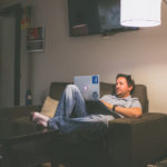 Man Sitting On Couch Looking At A Laptop