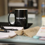 Office Desk With Papers, Pens And A Coffee Mug With The Caption Wework