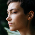 Woman In Front Of Green Tree With Her Eyes Closed In Deep Thought