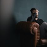 Man Sitting on Couch with Hand on Head