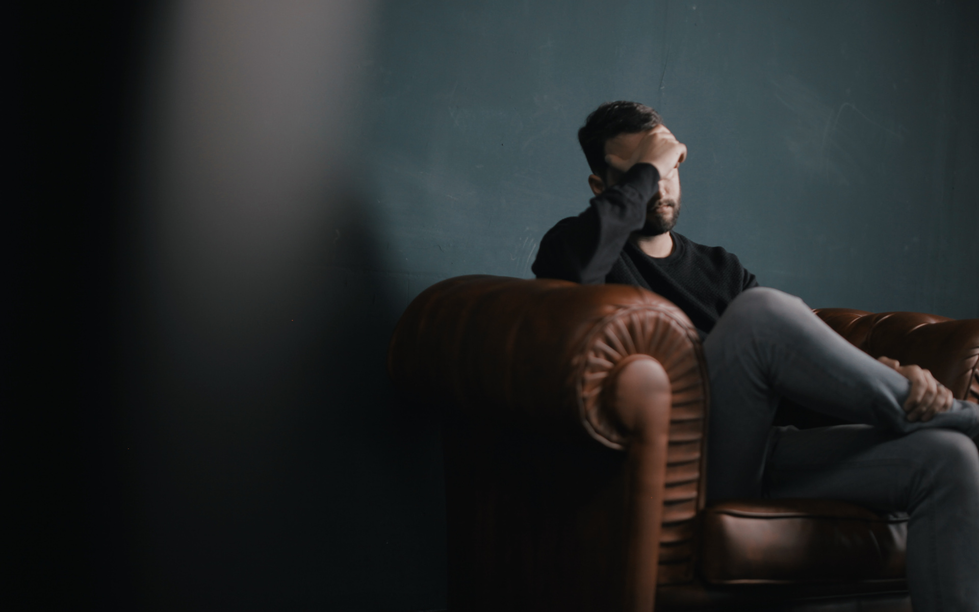 Man Sitting on Couch with Hand on Head